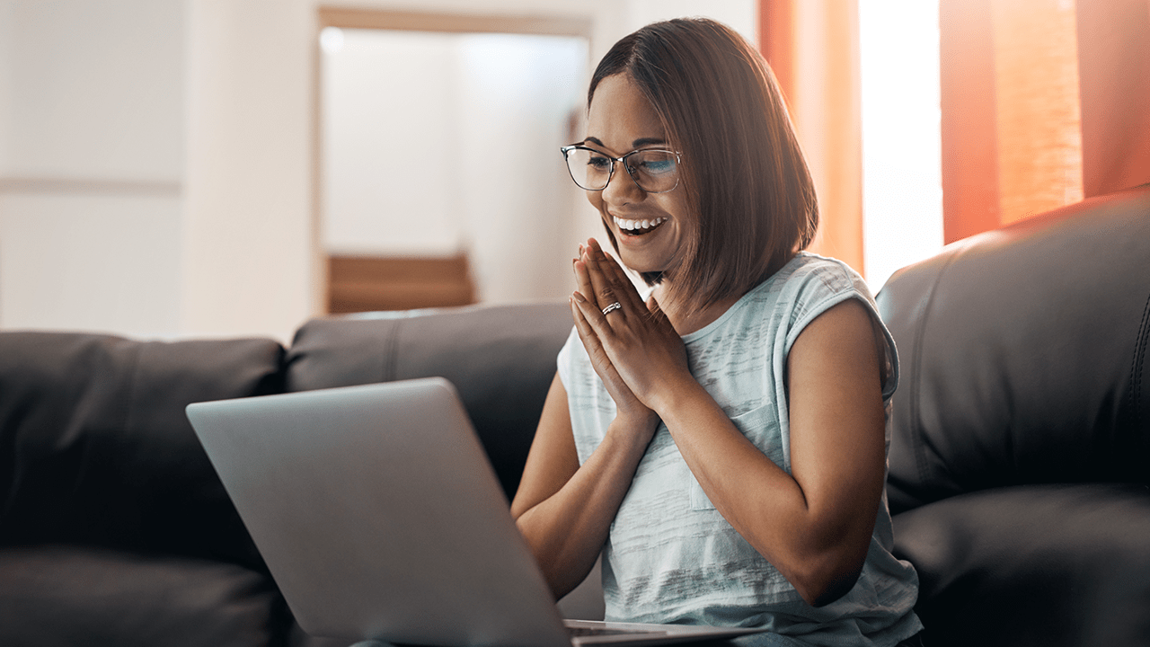 Afro American woman cheering and being excited while looking at laptop on her lap.
