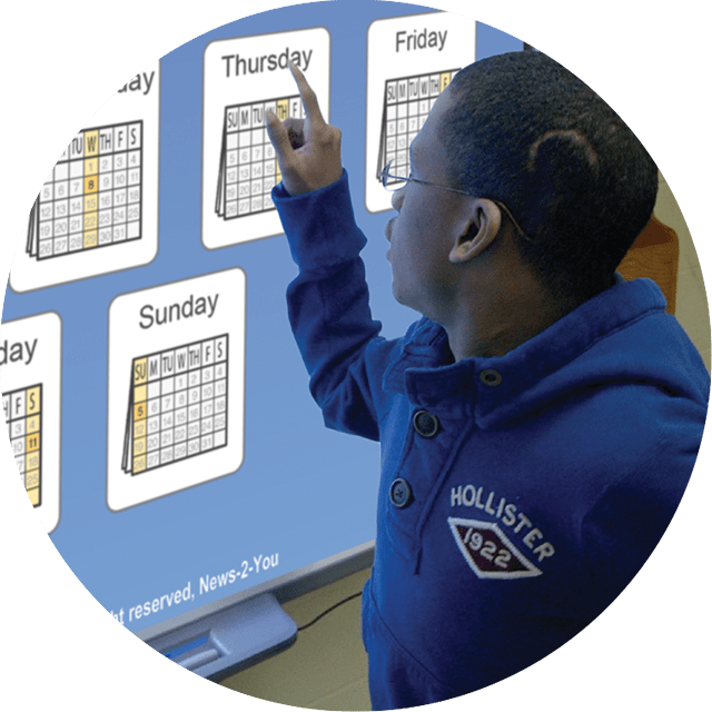 Student pointing at whiteboard screen with the days of the week.