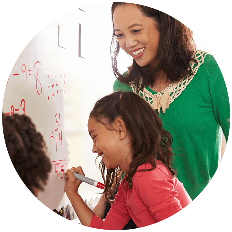 A teacher and elementary student working on addition on a whiteboard