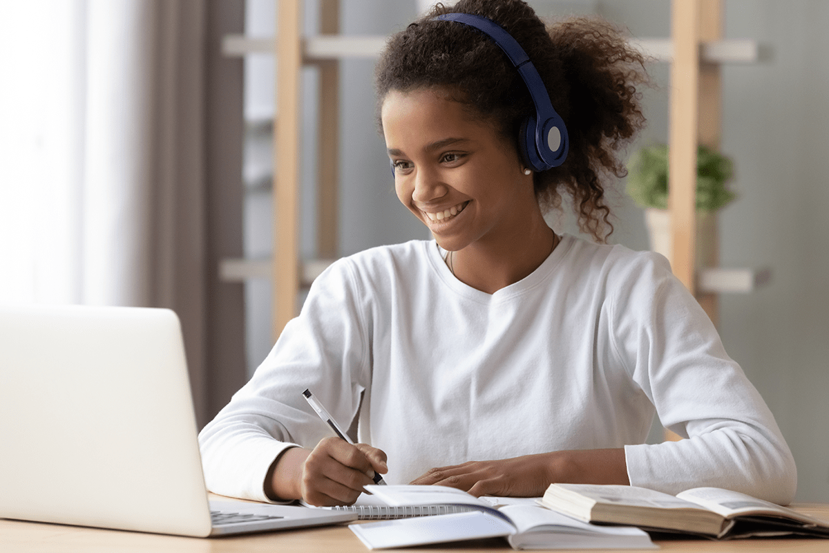 teenager with headphones taking notes while looking at a laptop